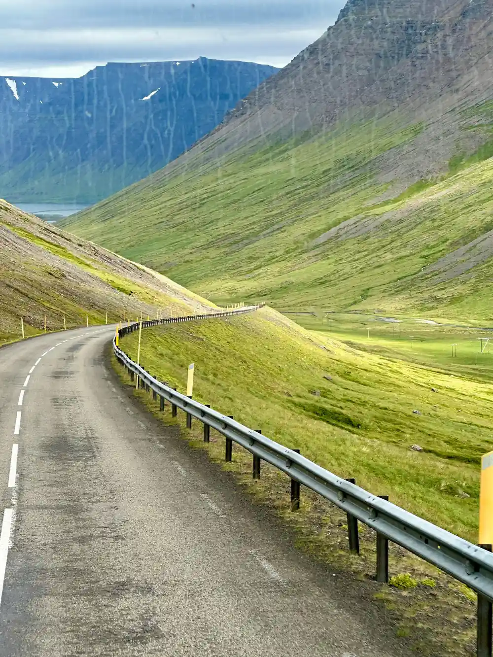 The empty road curving along a green valley behind a crash barrier