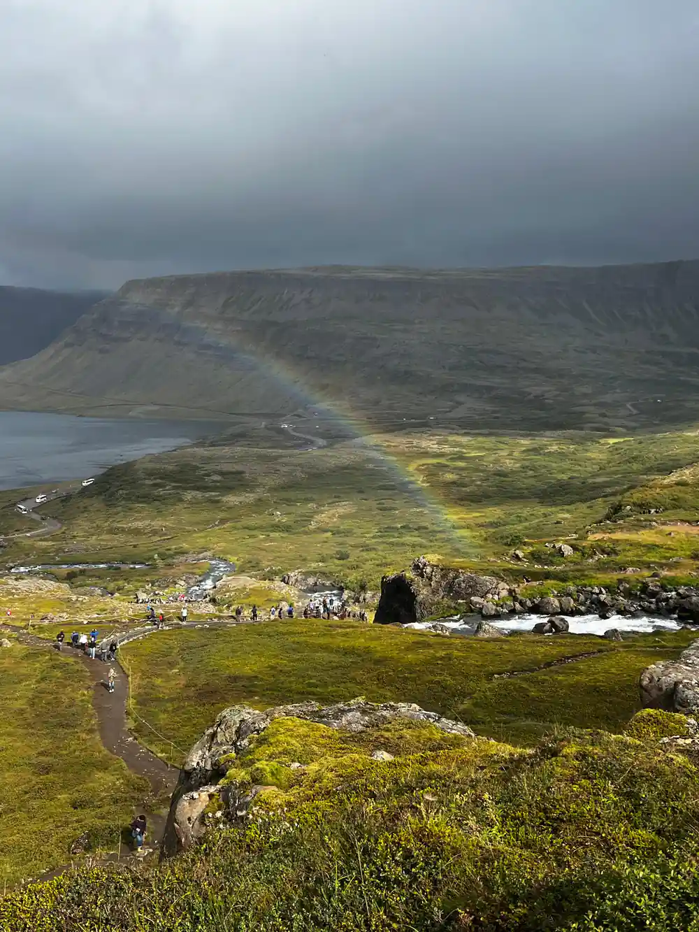 A faint rainbow over the fjord with the path in the foreground