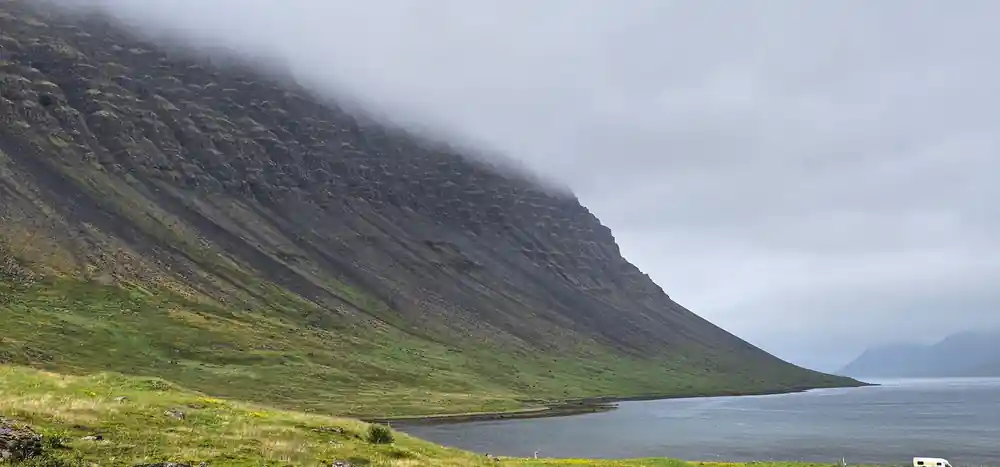 A long striped mountain wall dropping into the fjord in mist