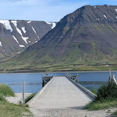 A wooden pier reaching into a Westfjords fjord below the mountains