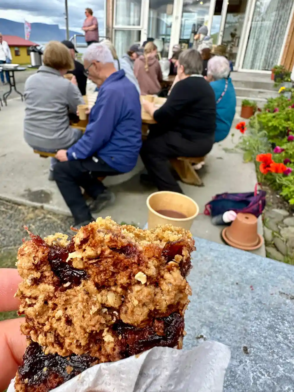 A slice of cake held up over a table of visitors outside the guesthouse